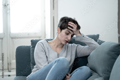 Attractive young woman looking down sad overwhelmed and lonely on the couch at home