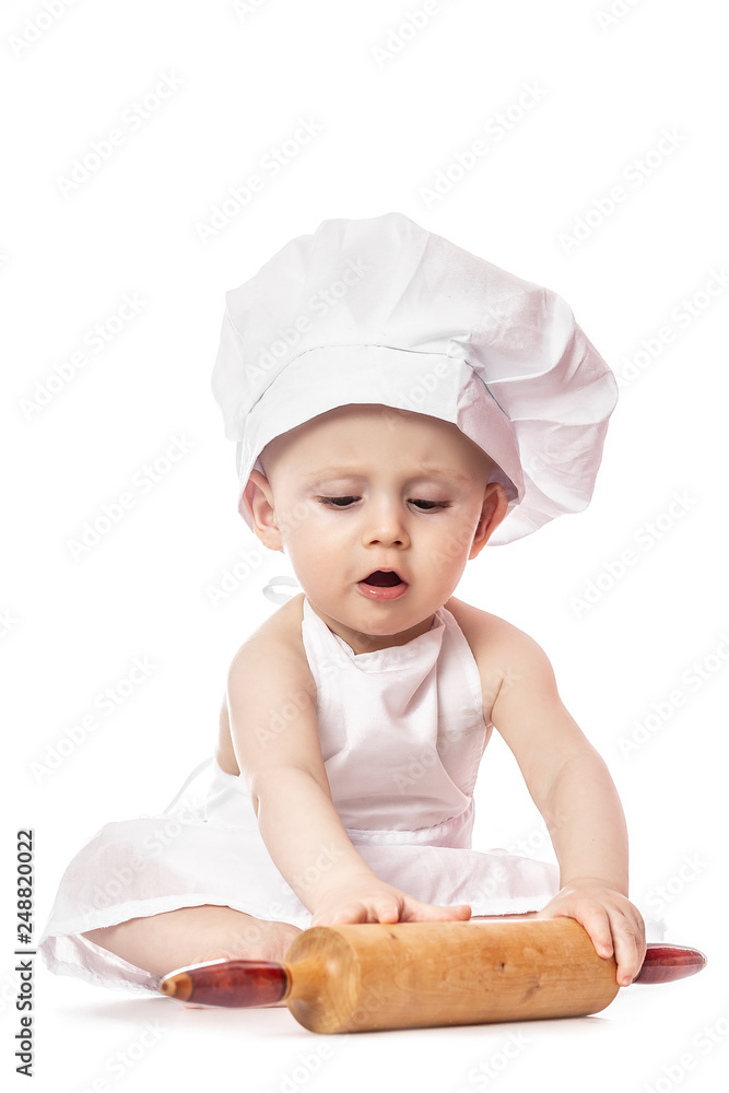 Infant cook baby portrait wearing apron and chef hat with dough rolling pin, isolated on a white background Infant cook baby portrait wearing apron and chef hat with dough rolling pin, isolated on a white background