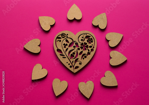Sunny hearts composition from top view on pink background. Poker-drawing wooden heart in the center.