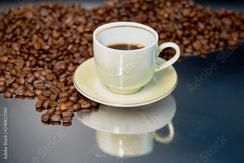 Cup of coffee and roasted coffee beans on reflective surface