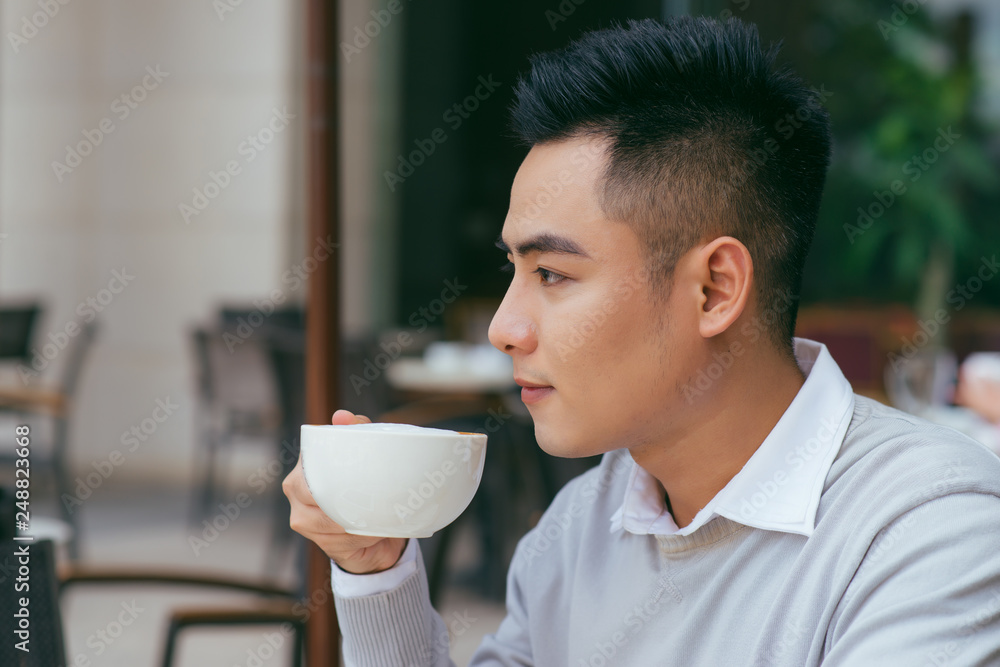 Starting new day in cafe. Side view of young Asian man holding coffee cup and looking away while sitting in cafe - Image Starting new day in cafe. Side view of young Asian man holding coffee cup and looking away while sitting in cafe - Image