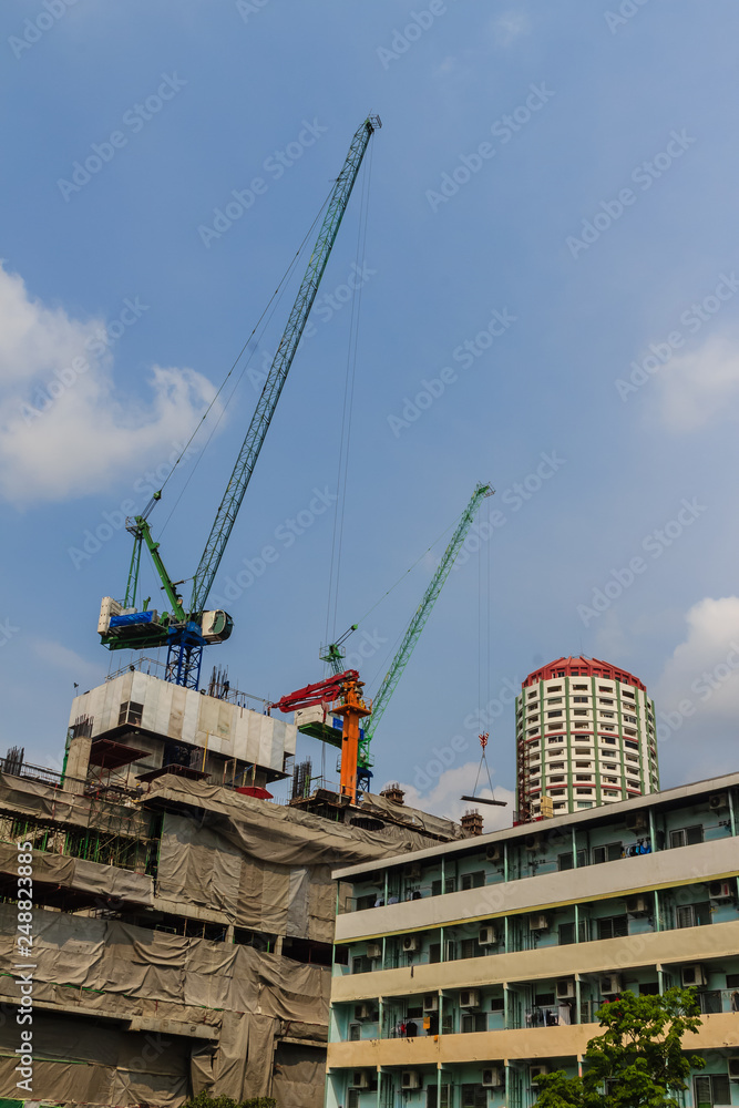 View of luffing jib tower crane at condominium construction site over steel framework among high rise buildings in the center of Bangkok, Thailand. View of luffing jib tower crane at condominium construction site over steel framework among high rise buildings in the center of Bangkok, Thailand.