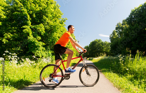 fitness, sport and healthy lifestyle concept - happy young man cycling by bicycle outdoors in summer park