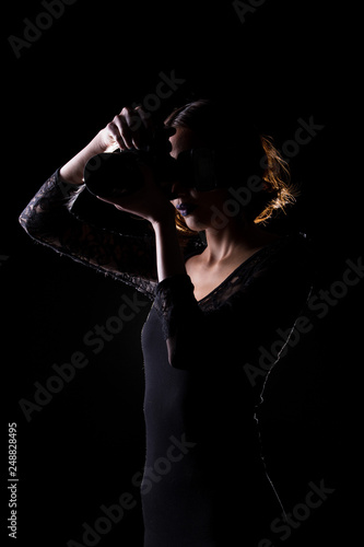 Asian Woman Photographer hold camera with external flash point to shoot subject, wear gray suit. studio lighting black background isolated low key exposure, reporter journalist take photo celebrity