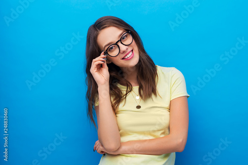 people concept - smiling young woman or teenage girl in yellow t-shirt and glasses over bright blue background