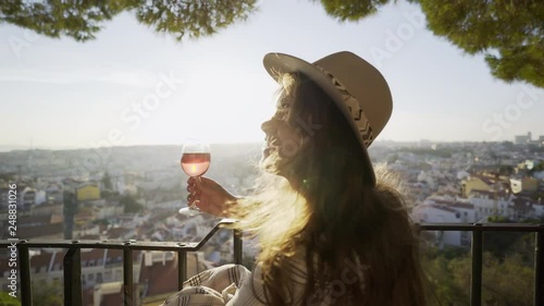 Side view of beautiful young female smiling and looking away while drinking good wine on terrace of outdoor cafe on sunny day