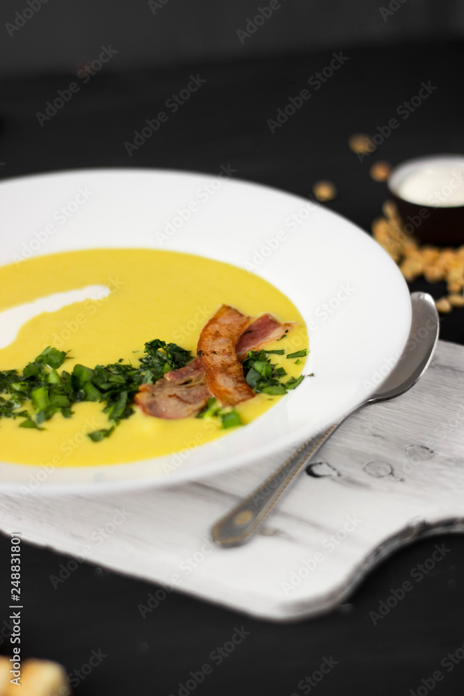 Pea soup with pieces of bacon, parsley and onion in a bowl on a dark background. Pea cream soup. Macro