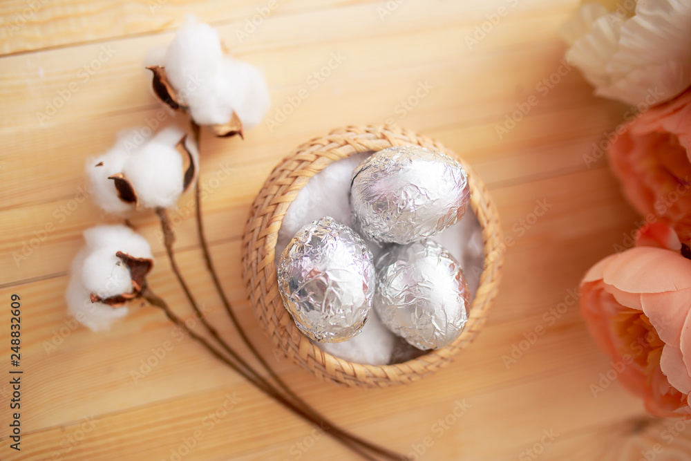 White eggs and eggs in foil on the wooden background with flowers and cotton around. Eggs in the basket