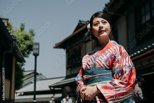gorgeous japanese young woman standing in old town on sunny day wearing kimono dress. beautiful lady in traditional cloth looking around in kiyomizu zaka street surrounding by wooden house kyoto.
