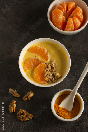 Tasty tangerine smoothie bowl with fruits, cereals, seeds and turmeric powder over grey background