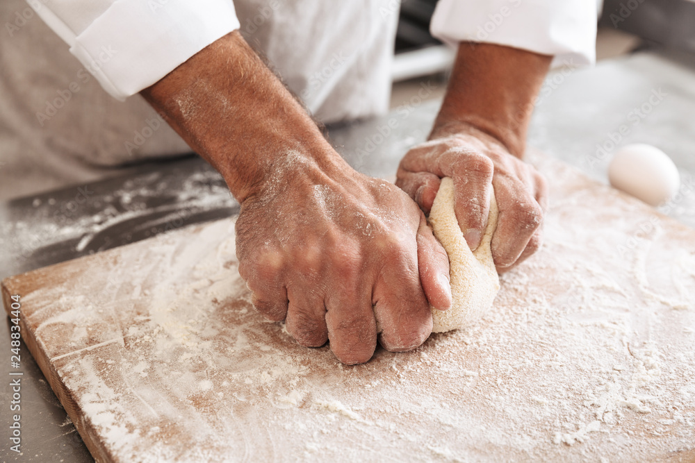 Cropped portrait of man chief making dough for bread, on table at bakery or kitchen