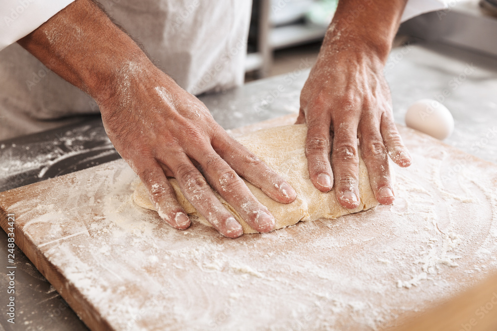 Closeup portrait of beautiful male hands making dough for bread, on table at bakery or kitchen
