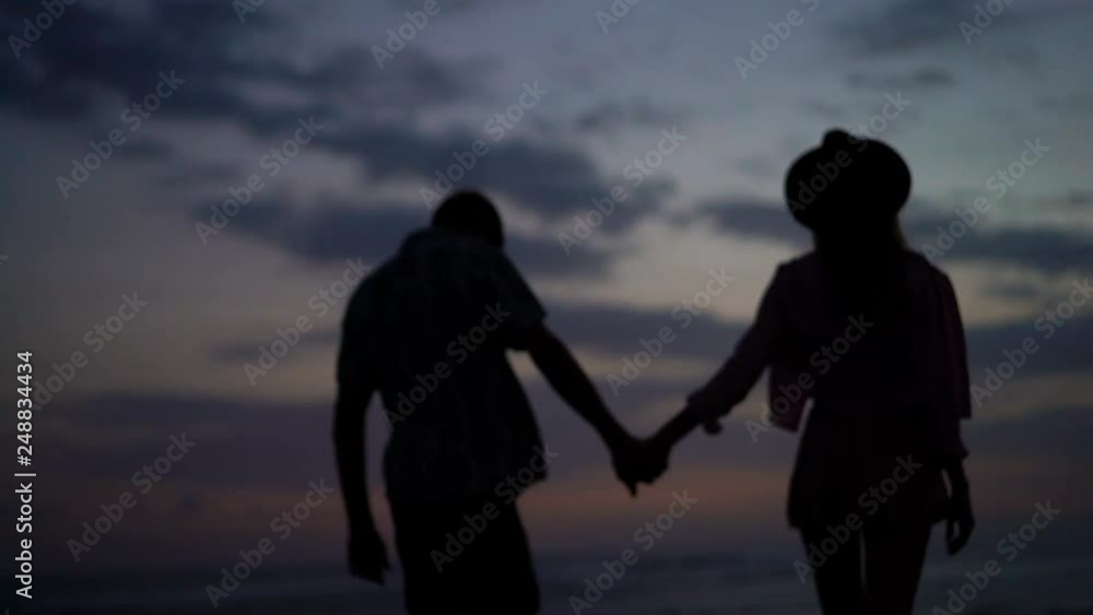 Young couple in love walking, holding hands during sunset on beach Young couple in love walking, holding hands during sunset on beach