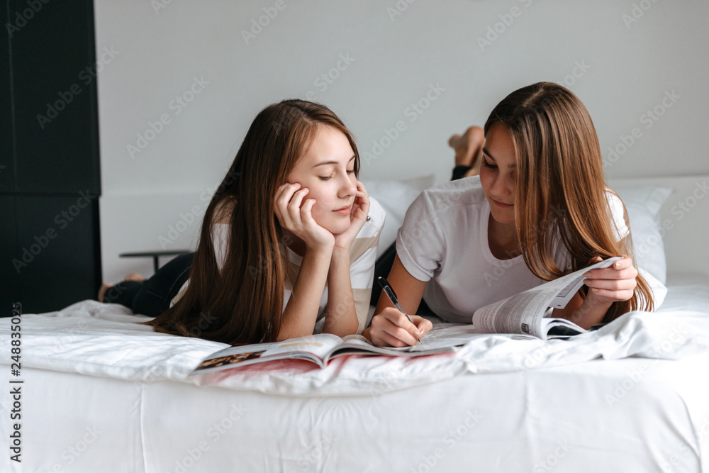 Two cheerful young teenage girls laying on bed, reading Two cheerful young teenage girls laying on bed, reading