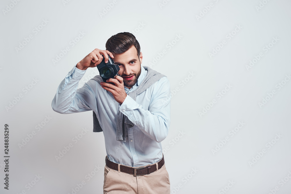 Nice shot. Attractive young man in casual wear is photographing you while standing in studio on a grey background Nice shot. Attractive young man in casual wear is photographing you while standing in studio on a grey background