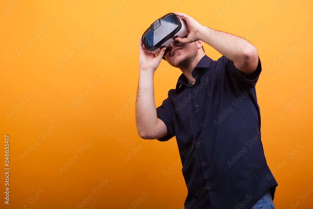 Young man in casual blue shirt with VR goggles over yellow background Young man in casual blue shirt with VR goggles over yellow background