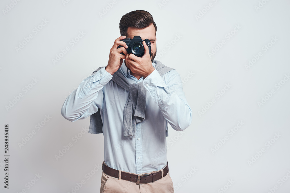 Do what you love. Young bearded man in blue shirt taking picture with camera isolated on grey background. Do what you love. Young bearded man in blue shirt taking picture with camera isolated on grey background.