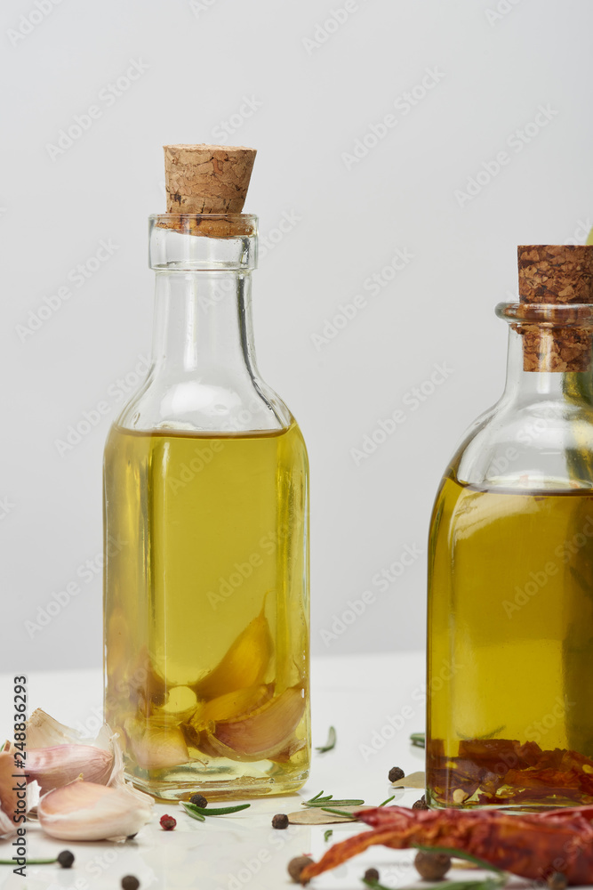 various bottles of oil flavored with different spices and rosemary on white surface various bottles of oil flavored with different spices and rosemary on white surface