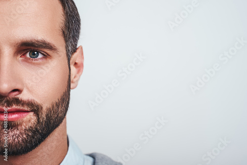 Close-up half face portrait of a smiling attractive man with a stubble looking at camera