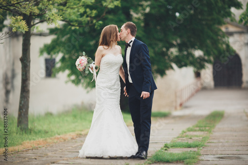 Beautiful couple of happy stylish newlyweds walking in the park on their wedding day with bouquet