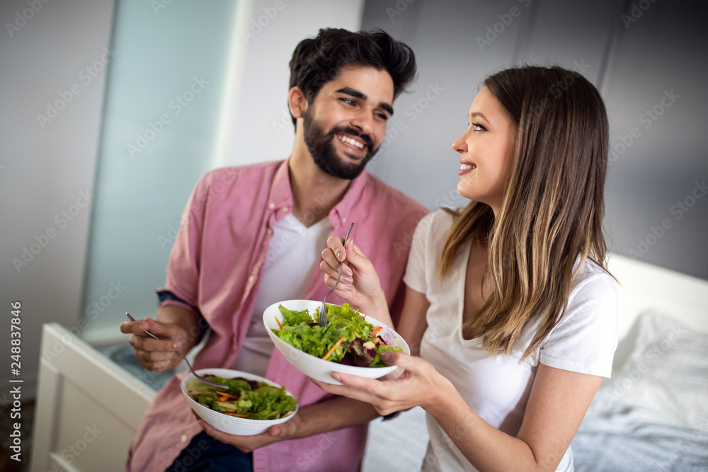 Beautiful young playful couple eating salad together at home Beautiful young playful couple eating salad together at home