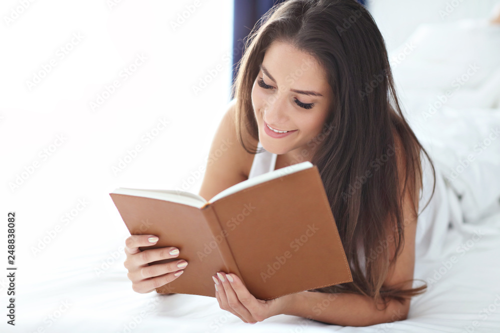 Young beautiful woman resting in bed with book Young beautiful woman resting in bed with book