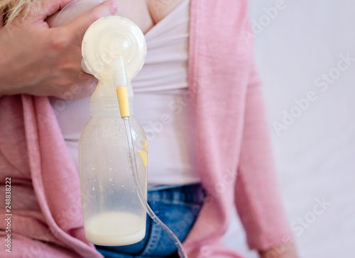 Young mother is using single electric breast milk pump and pumping breast milk for her baby. Breast milk for supplementary feeding, infant nutrition. - image photo