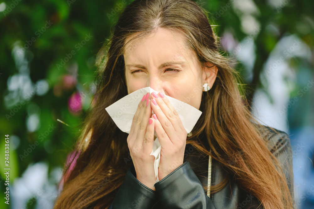 Young woman blowing her nose affected by spring allergy to pollen in a garden, with sinus problems Young woman blowing her nose affected by spring allergy to pollen in a garden, with sinus problems