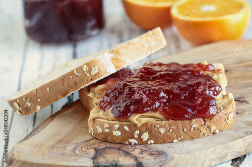 Homemade Peanut Butter and Jelly Sandwich on oat bread, over a rustic wooden background with fruit in the background ready for lunch.