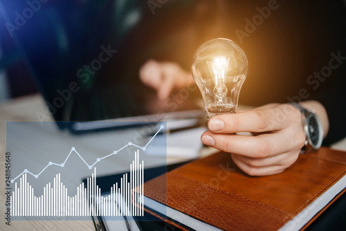 Business women hand holding light bulb, concept of new ideas with innovation and creativity. Concept of virtual diagram,graph interfaces,digital display,connections,statistics icons