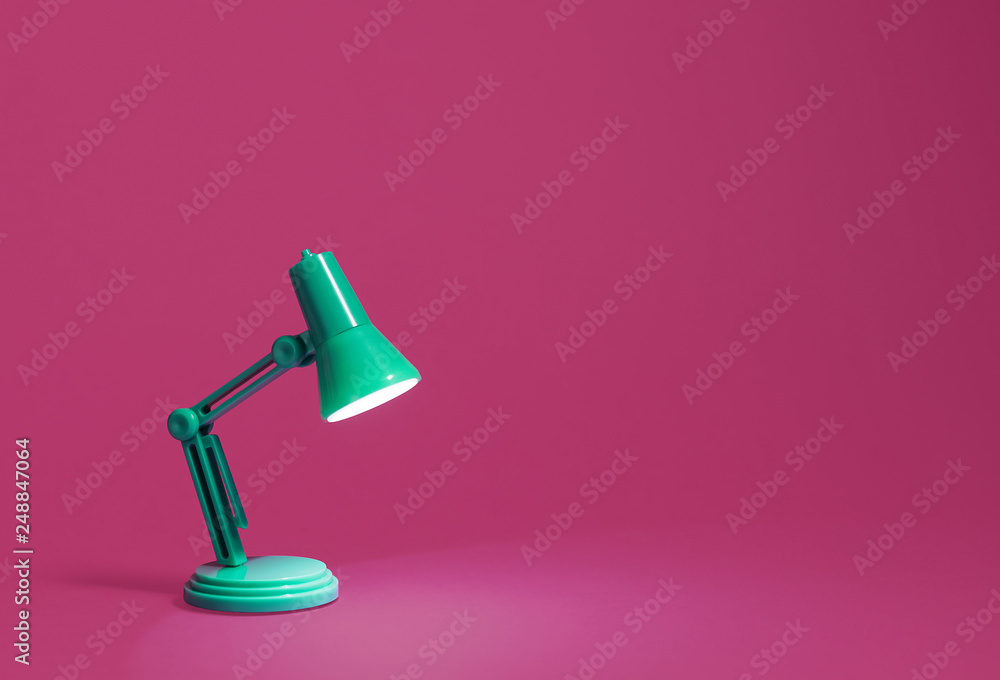 Retro green desk lamp turned on and bent over shining on a bright pink background.  Landscape orientation with a left side composition leaving room for text and copy space. - obrazy, fototapety, plakaty 