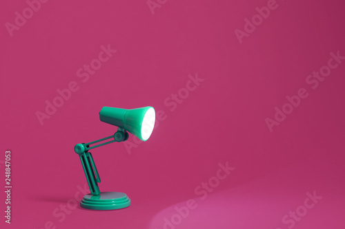 Vintage green desk lamp on a bright pink background.  Lamp turned on and shining out to the edge of the image.  Copy space and room for text.