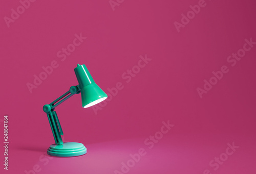 Retro green desk lamp turned on and bent over shining on a bright pink background.  Landscape orientation with a left side composition leaving room for text and copy space. photo