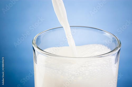 Pouring fresh milk into glass on a blue background