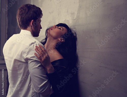 Sexy couple portrait. Man in white shirt kissing his sensual beautiful girlfriend in neck with much emotion. Toned closeup portrait photo
