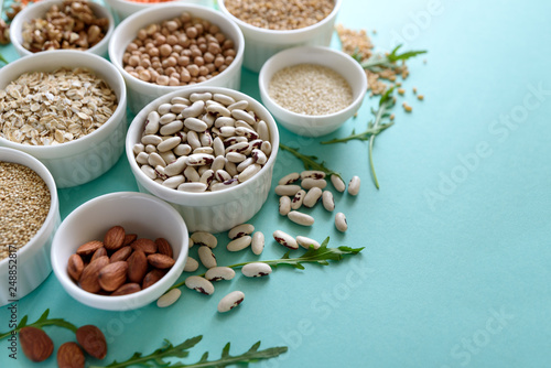 Set of bowls with organic quinoa  lentil  chickpea  wheat  walnut  almond  hazelnut and sesame. Cereals and legumes assortment on blue paper background. Top view. Copy space. Flat lay