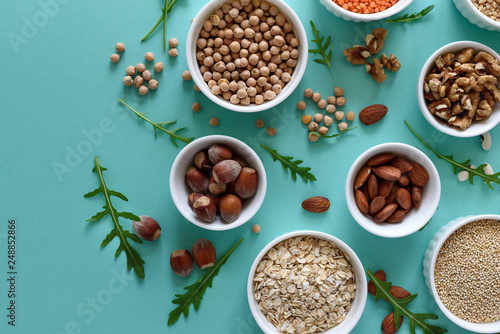Set of bowls with organic quinoa  lentil  chickpea  wheat  walnut  almond  hazelnut and sesame. Cereals and legumes assortment on blue paper background. Top view. Copy space. Flat lay