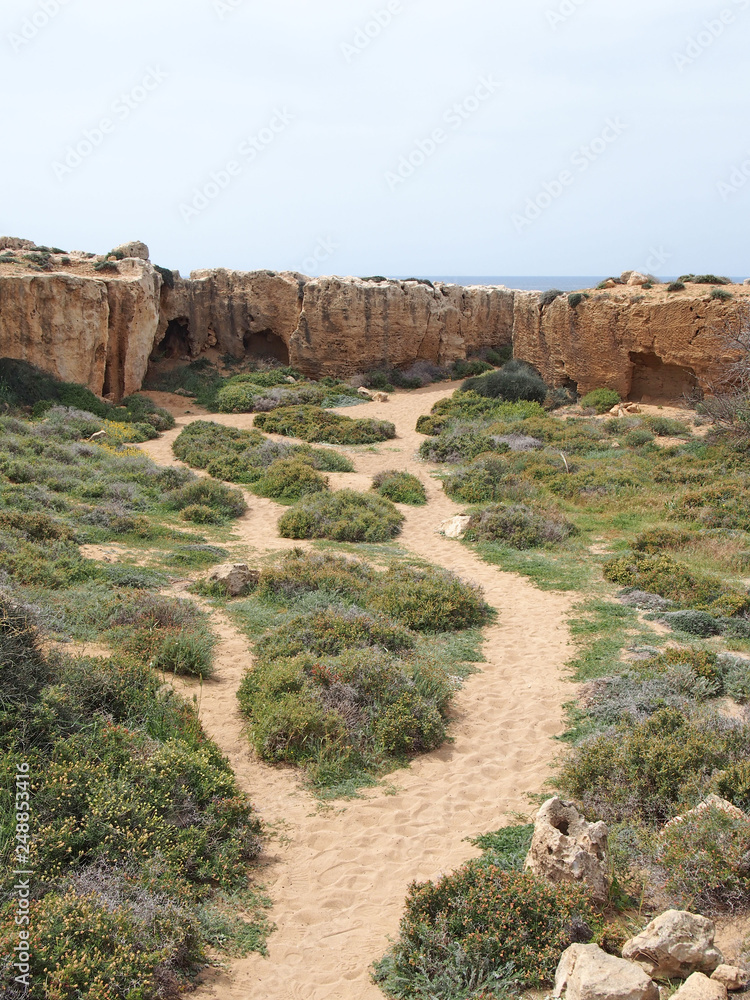 a path leading to caves and graves carved into the rock face near the sea at the tomb of the kings area in paphos cyprus