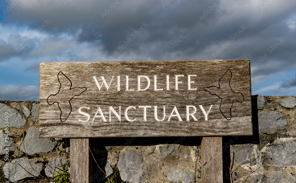Fototapeta premium Wildlife sactuary sign outside stone wall barrier