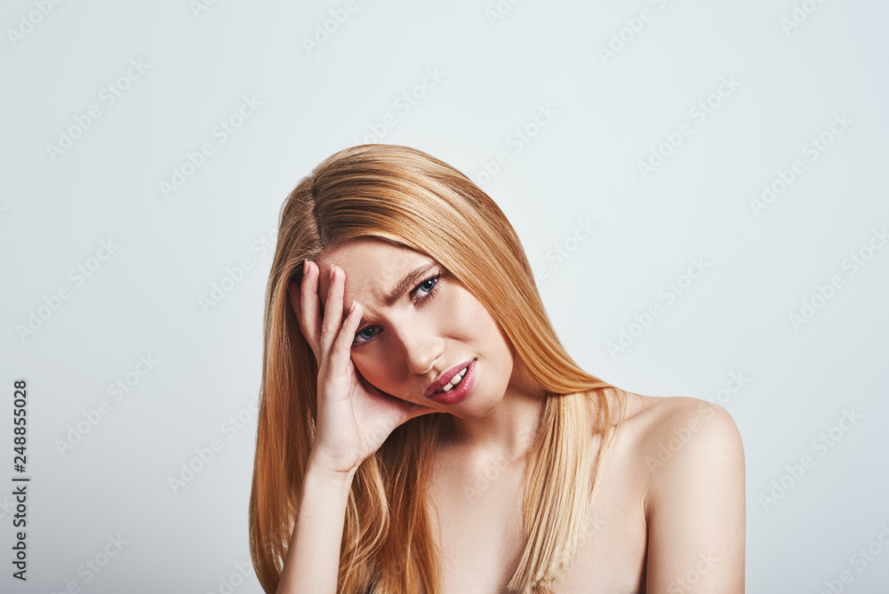 Obraz premium In pain. Studio shot of frustrated blonde woman making a face and keeping hand on head. Grey background