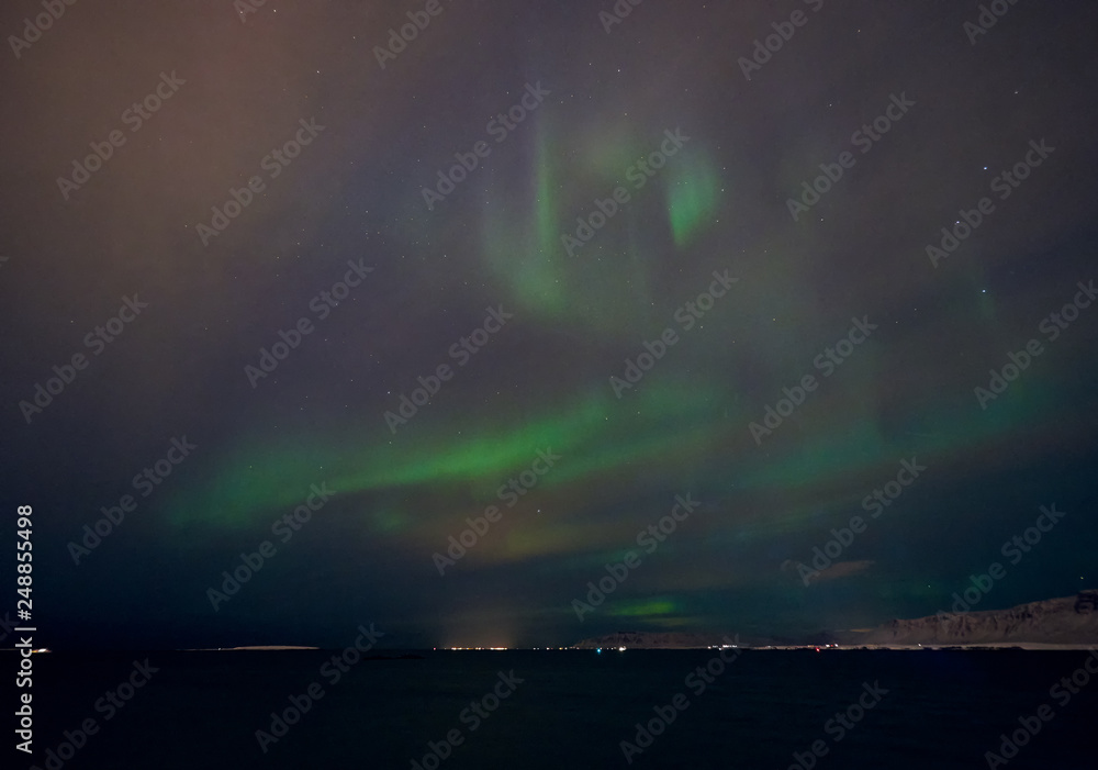 View of the northern lights from the coast in Reykjavik, Iceland, on a night with wind and clouds