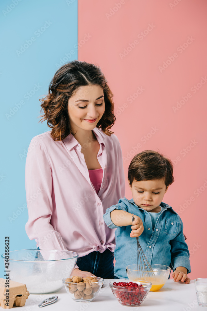 cute little boy whipping eggs while happy mom looking at him with smile on bicolor background on bicolor background cute little boy whipping eggs while happy mom looking at him with smile on bicolor background on bicolor background