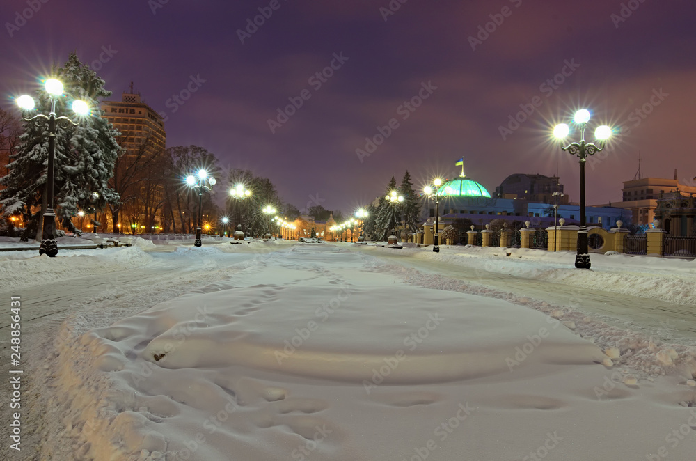 KYIV, UKRAINE-JANUARY 27, 2019: Winter landscape of snow-covered square with two rows of lanterns in front of the Verkhovna Rada of Ukraine. Mariinsky Park and Hotel Kyiv on the background