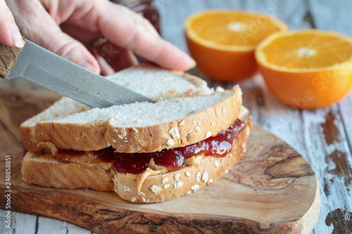 Womans hand cutting a peanut butter and Jelly sandwich on a rustic wooden cutting board. Selective focus on sandwich. photo