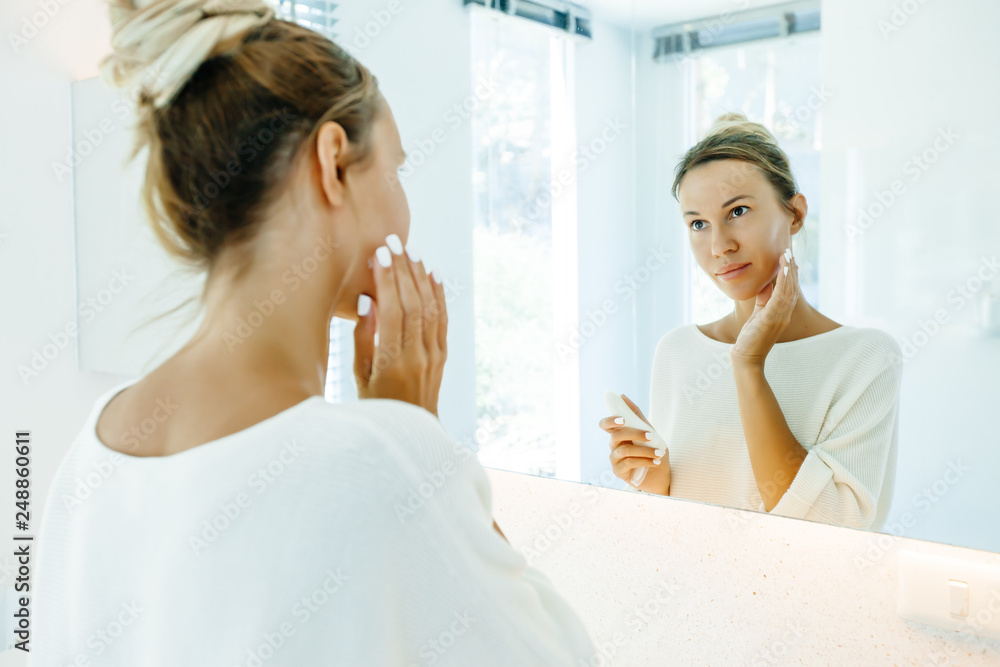 Woman applying face cream in bathroom Woman applying face cream in bathroom