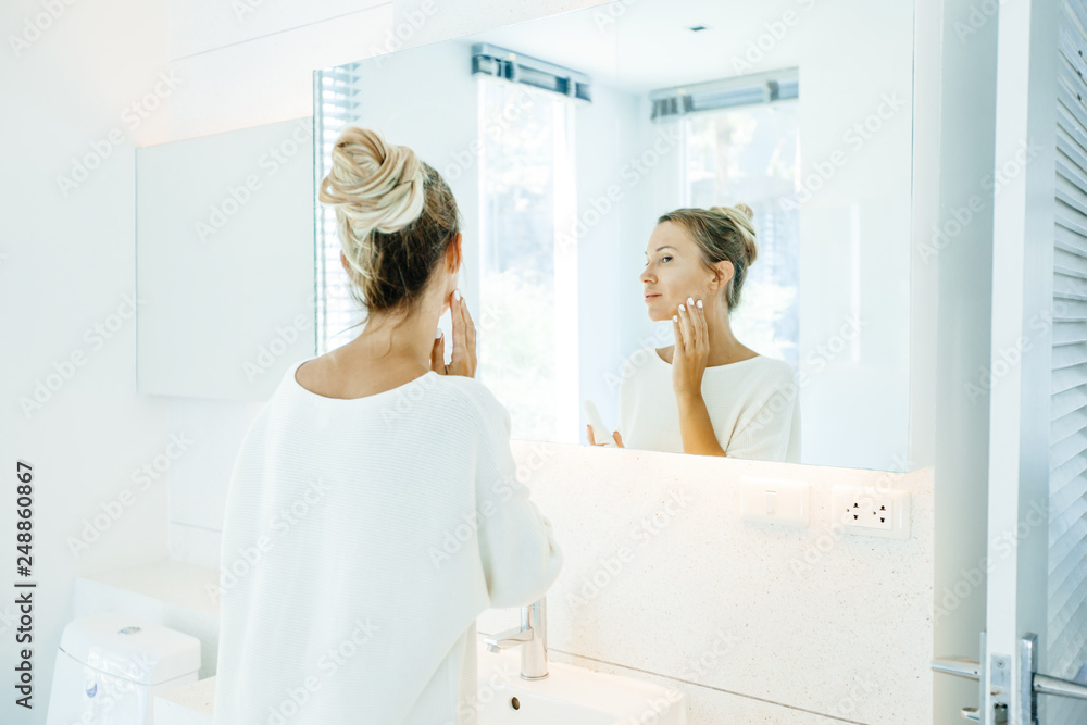 Obraz premium Woman applying face cream in bathroom