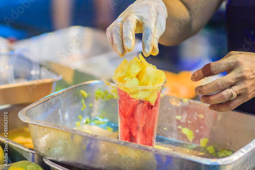 Close up street fruit vendor during slicing fruits and arrange in plastic cup for sale at Khao San Road night market, Bangkok, Thailand. photo