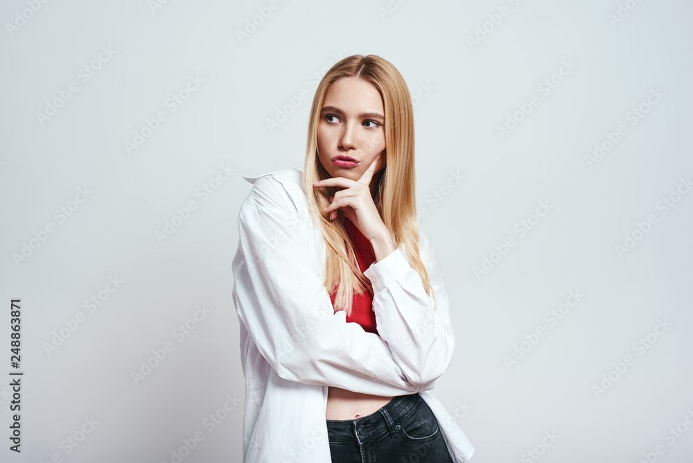 Stubborn girl. Studio portrait of cute blonde woman touching her chin and making a face while standing in studio on a grey background. Stubborn girl. Studio portrait of cute blonde woman touching her chin and making a face while standing in studio on a grey background.
