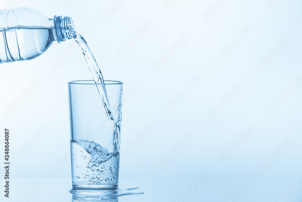 Pouring water from bottle into glass on blue background. Photo with copy space. Pouring water from bottle into glass on blue background. Photo with copy space.