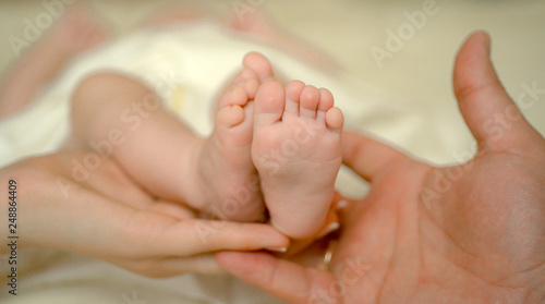 Mother and father hold newborn baby bare feet. Tiny feet in woman hand. Cozy morning at home. Love and family concept.